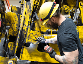 Two workers wearing hard hats and safety vests are working with machinery at a factory.