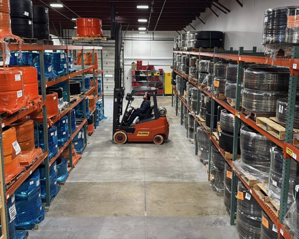 A person is pushing a forklift through an industrial warehouse filled with shelves of products.