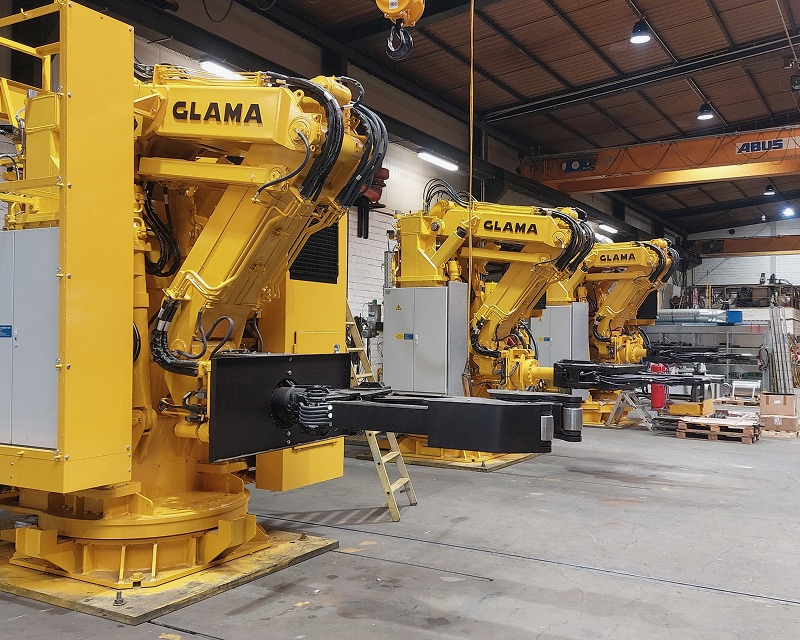 The blurred factory scene contains yellow machinery and a partially obscured text "GLAMA".