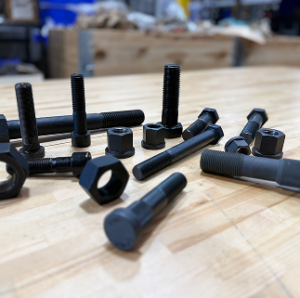 Black bolts and nuts scattered across a workbench with blurred background.