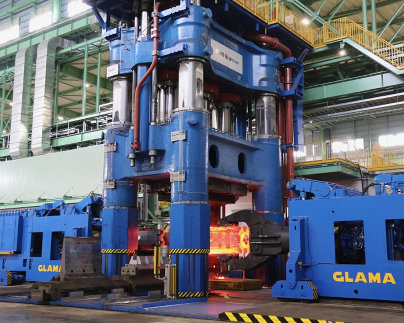 A blue machine with yellow caution stripes is surrounded by a factory environment.