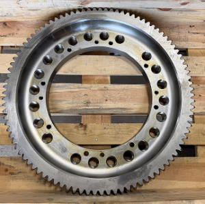 A large metal gear with holes is placed against a wooden background.